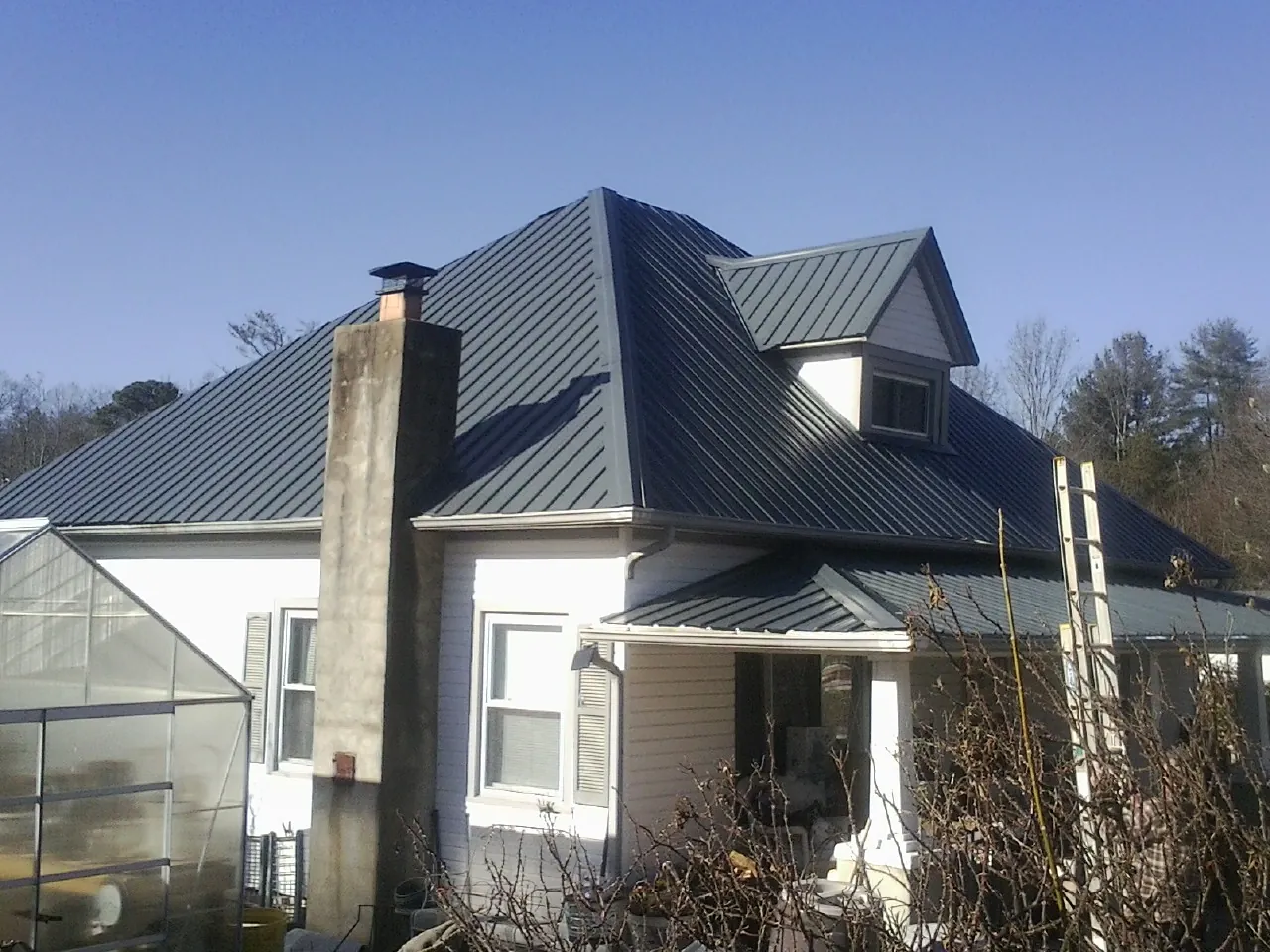 Dark blue standing seam metal roof on a white farmhouse with dormer — Slate & Tile Roof Repair by Roofing Brothers in Cleburne