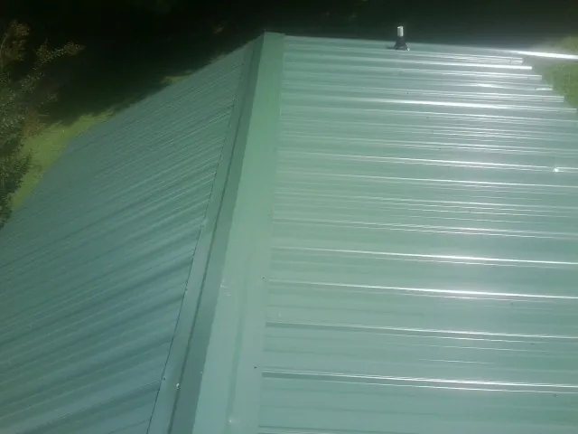New green metal panels meeting at the ridge of a roof — Flat Roof Repair work by our crew in Cleburne