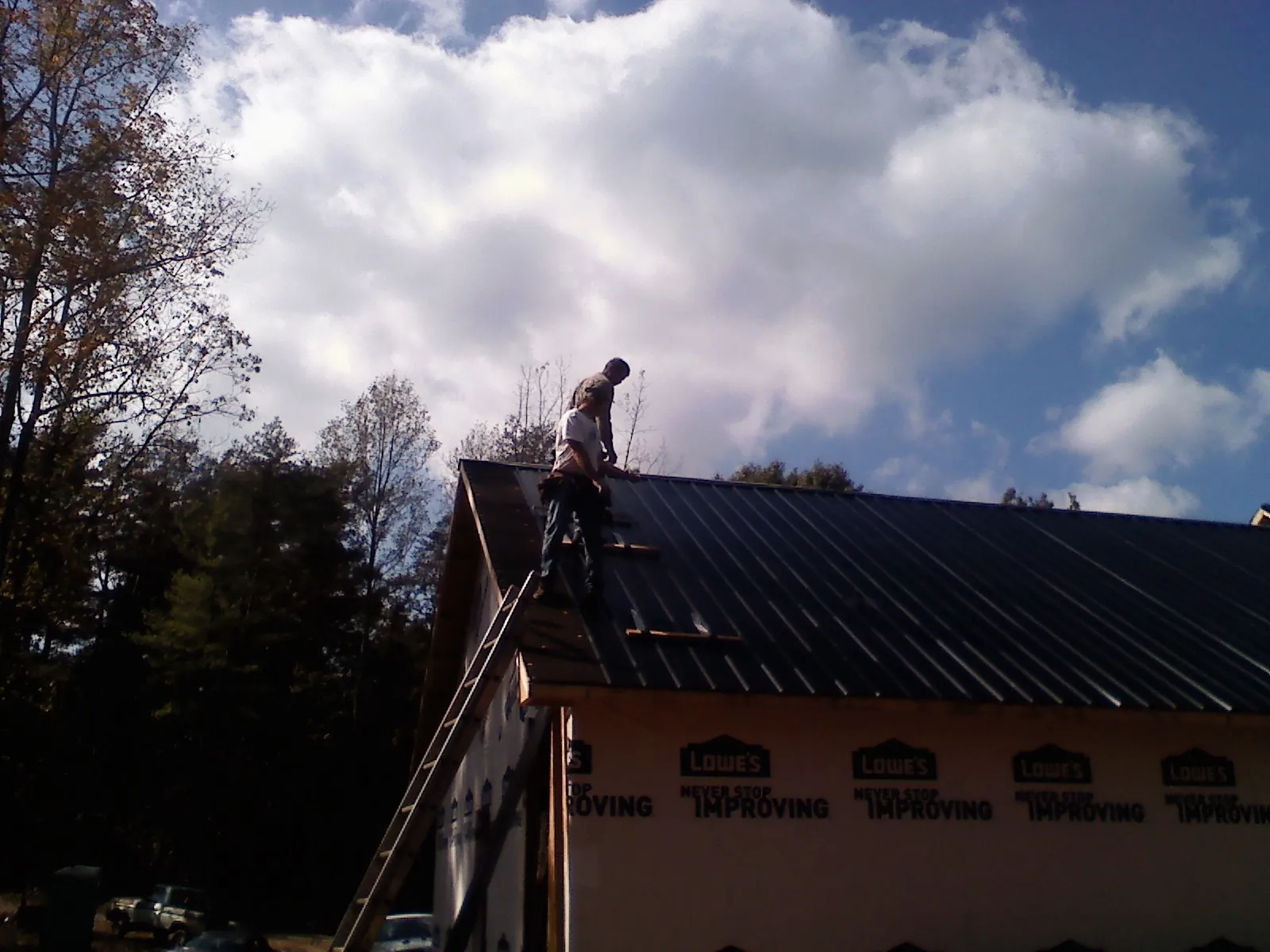 Roofer fastening dark metal panels high against a cloudy sky, from a Roof Inspection job in Cleburne