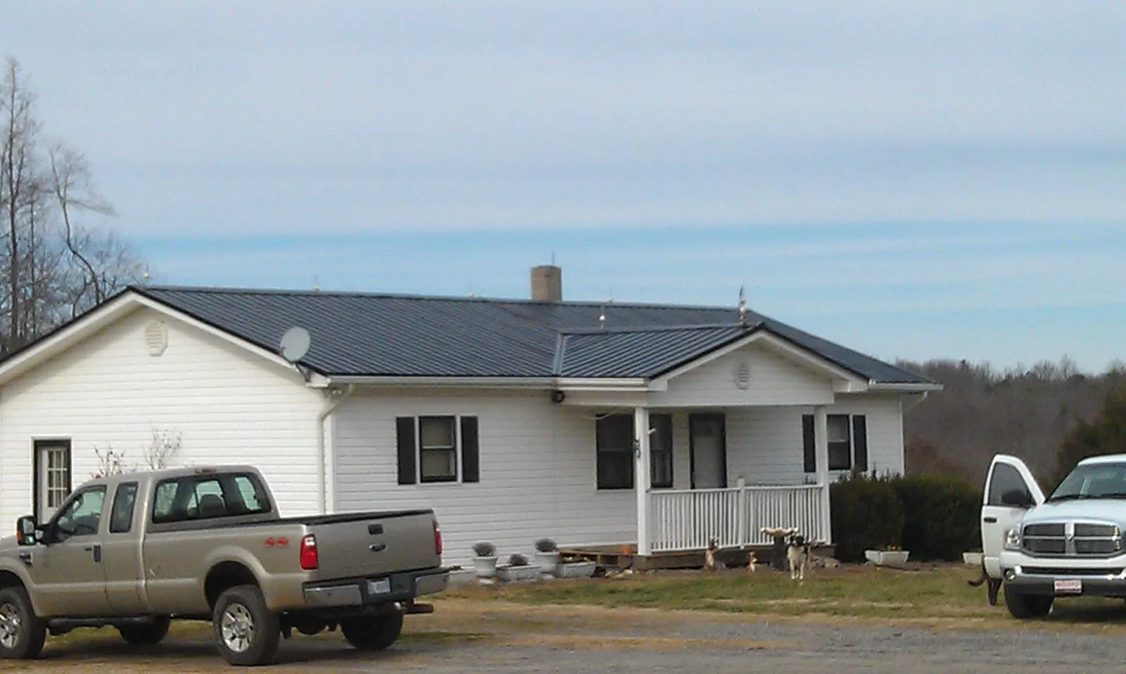 Finished dark metal roof on a white ranch home with work trucks parked in Cleburne